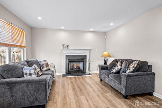 living area featuring a lit fireplace, recessed lighting, baseboards, and light wood-style floors