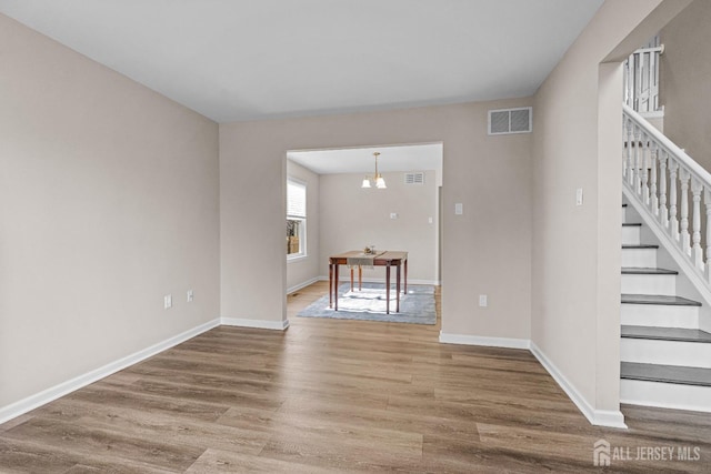 unfurnished living room featuring visible vents, baseboards, wood finished floors, and stairway