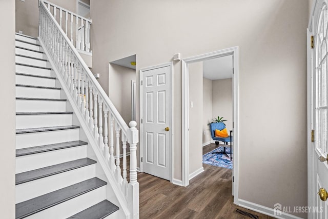 stairway featuring visible vents, a towering ceiling, baseboards, and wood finished floors