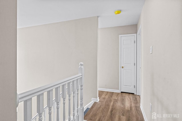 corridor featuring baseboards, an upstairs landing, and wood finished floors