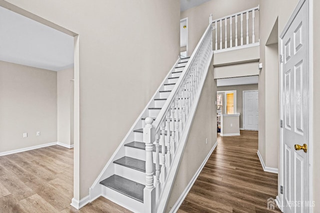 staircase featuring baseboards, wood finished floors, and a towering ceiling