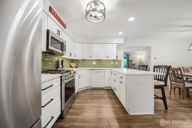 30 Forest Garden Dr, Old Bridge, NJ 07747 - kitchen featuring appliances with stainless steel finishes, a peninsula, a kitchen bar, backsplash, and dark wood-style flooring