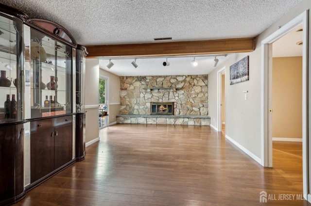 9 Merion Dr, Manalapan, NJ 07726 - unfurnished living room featuring baseboards, track lighting, dark wood-style floors, a textured ceiling, and a stone fireplace