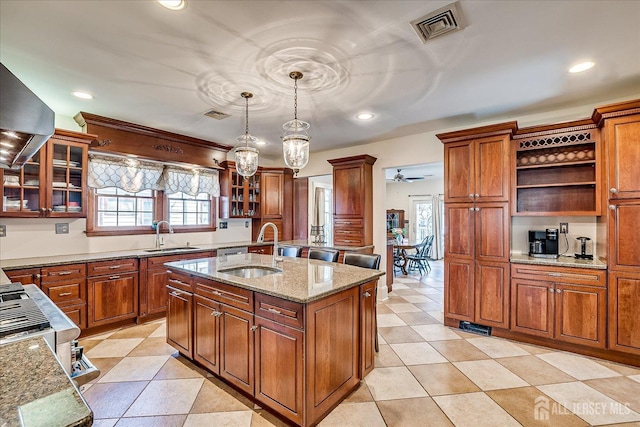 kitchen featuring visible vents, a sink, light stone countertops, a center island with sink, and open shelves