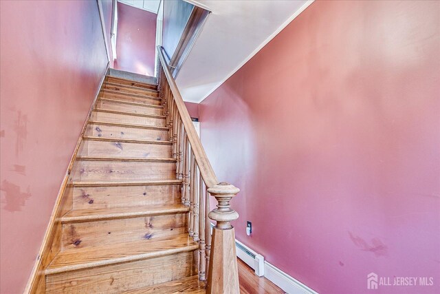 stairway with baseboard heating, wood finished floors, baseboards, and ornamental molding