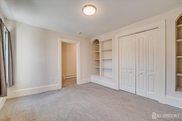 unfurnished bedroom with a baseboard heating unit, a closet, baseboards, and carpet floors