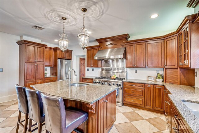 kitchen with visible vents, light stone counters, range hood, stainless steel appliances, and a sink