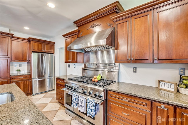 kitchen featuring brown cabinetry, wall chimney range hood, light stone countertops, and stainless steel appliances