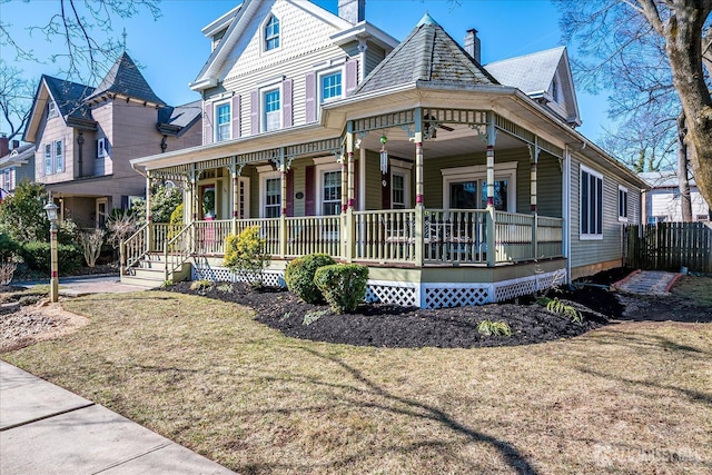 victorian-style house featuring a chimney, a front lawn, fence, and covered porch