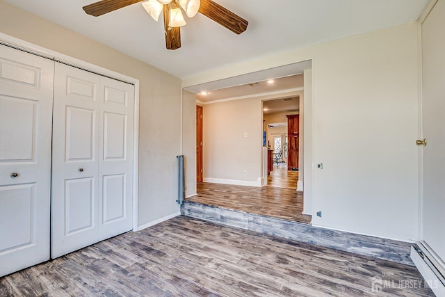 unfurnished bedroom featuring baseboards, a ceiling fan, wood finished floors, a closet, and a baseboard radiator