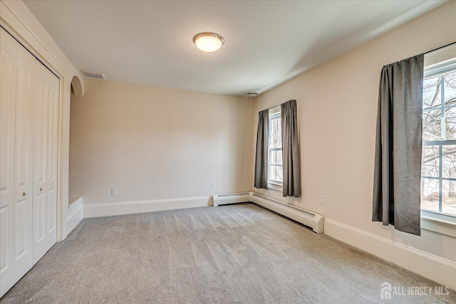 unfurnished bedroom with a baseboard heating unit, visible vents, carpet flooring, and multiple windows