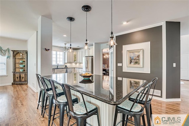 kitchen featuring stainless steel appliances, white cabinets, backsplash, decorative light fixtures, and light wood-type flooring