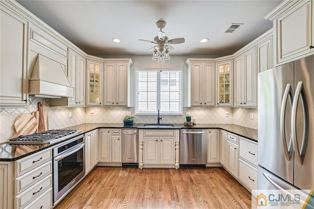 kitchen with light hardwood / wood-style flooring, backsplash, stainless steel appliances, custom exhaust hood, and sink