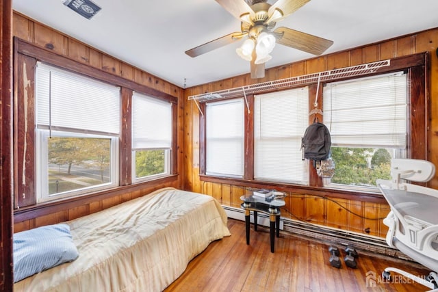 bedroom featuring ceiling fan, wood walls, and wood-type flooring