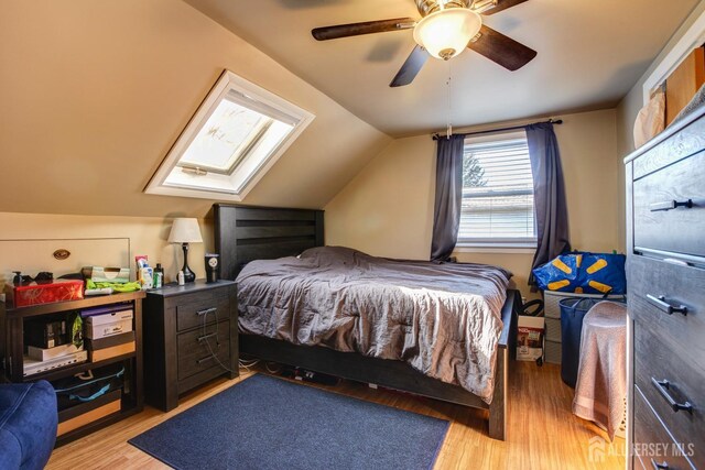 bedroom featuring ceiling fan, vaulted ceiling with skylight, and light wood-type flooring