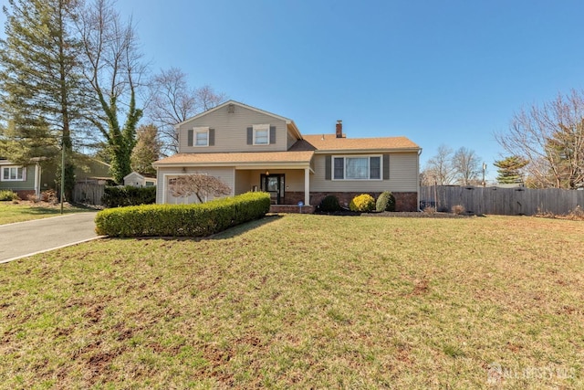 tri-level home featuring a chimney, driveway, a front yard, brick siding, and fence