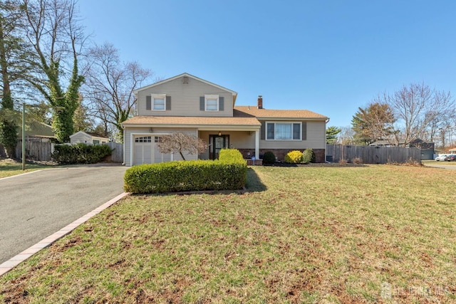 split level home with a chimney, driveway, a front lawn, a garage, and fence