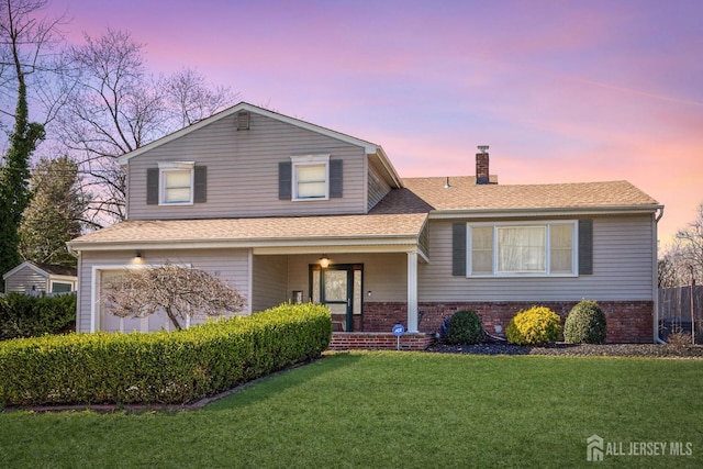 tri-level home featuring roof with shingles, a chimney, a front lawn, and brick siding