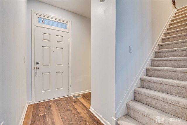 entrance foyer featuring visible vents, stairway, baseboards, and wood finished floors