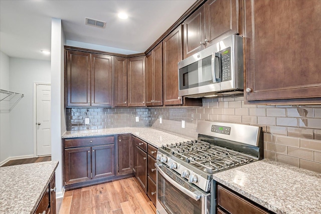 kitchen featuring stainless steel appliances, visible vents, decorative backsplash, light wood-style floors, and dark brown cabinetry