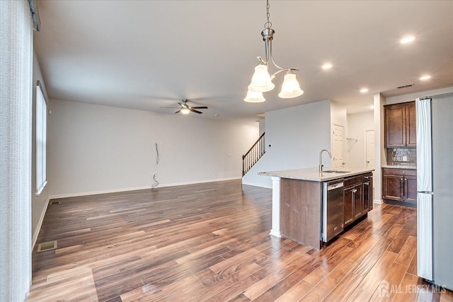 kitchen with pendant lighting, stainless steel appliances, backsplash, a sink, and wood finished floors