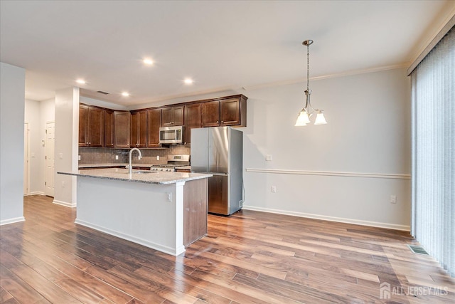 kitchen featuring light stone counters, decorative backsplash, appliances with stainless steel finishes, a sink, and wood finished floors