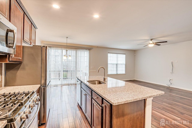 kitchen with wood finished floors, appliances with stainless steel finishes, a sink, and light stone counters