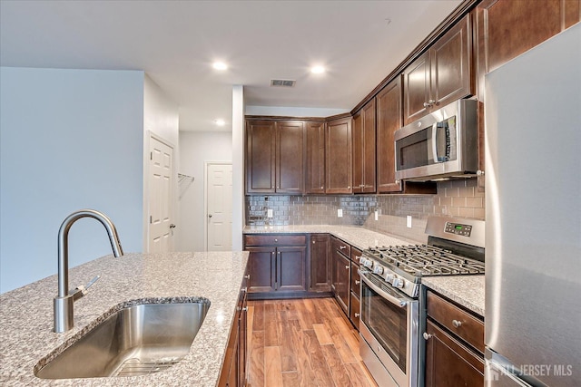 kitchen featuring stainless steel appliances, a sink, visible vents, light wood finished floors, and tasteful backsplash