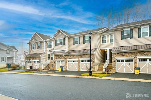 multi unit property with stone siding, driveway, a standing seam roof, and a residential view