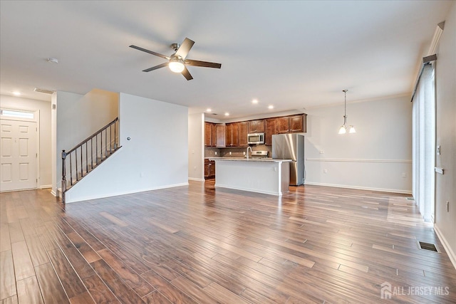 unfurnished living room with baseboards, visible vents, dark wood-type flooring, stairs, and ceiling fan with notable chandelier