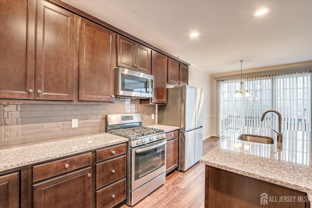 kitchen featuring light stone counters, stainless steel appliances, a sink, light wood-type flooring, and decorative backsplash