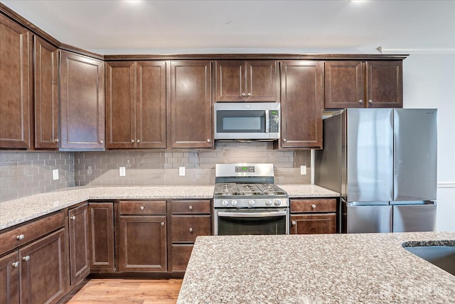 kitchen with light stone counters, appliances with stainless steel finishes, light wood-style flooring, and tasteful backsplash