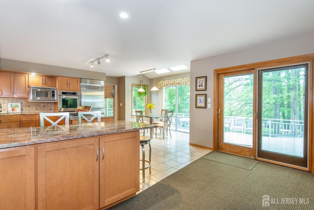 13 Clinton Ave, Edison, NJ 08820 - kitchen featuring built in appliances, a breakfast bar, tasteful backsplash, light tile patterned floors, and light stone counters