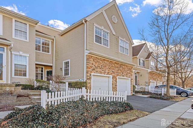 view of property featuring stone siding, driveway, a garage, and fence