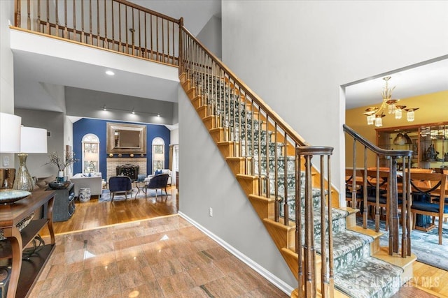 stairs featuring baseboards, a high ceiling, a brick fireplace, and wood finished floors