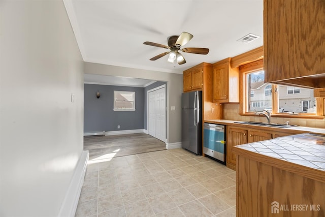 kitchen featuring a sink, baseboards, ceiling fan, tile counters, and appliances with stainless steel finishes