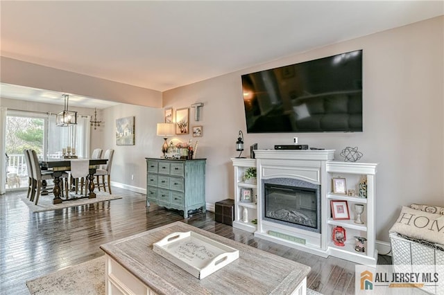 living room featuring dark wood-style flooring, baseboards, a chandelier, and a glass covered fireplace
