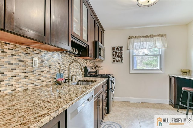kitchen with appliances with stainless steel finishes, dark brown cabinetry, baseboards, tasteful backsplash, and light stone countertops