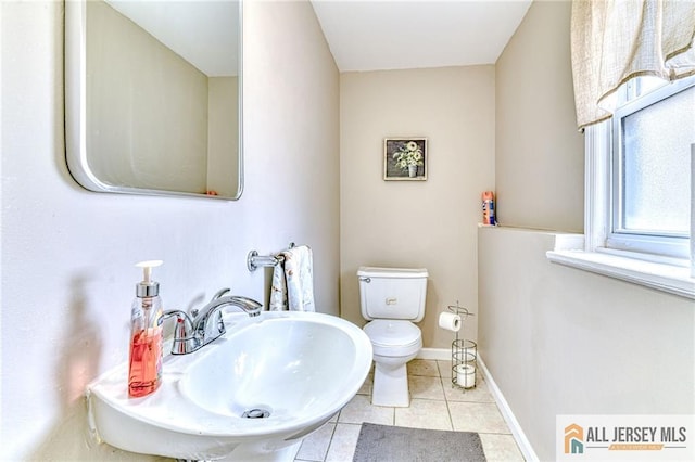 half bathroom with tile patterned flooring, toilet, a sink, and baseboards