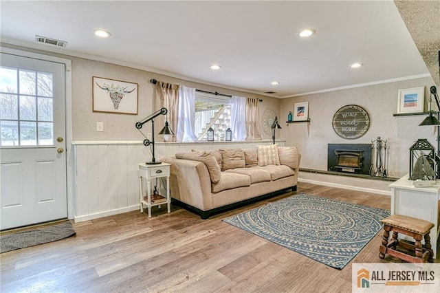 living room with crown molding, wood finished floors, a wainscoted wall, recessed lighting, and a fireplace with raised hearth