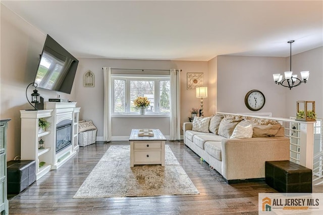 living room featuring plenty of natural light, a chandelier, wood finished floors, and a glass covered fireplace