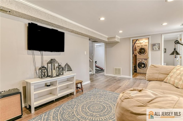 living room with stacked washer / dryer, stairs, wood finished floors, ornamental molding, and recessed lighting