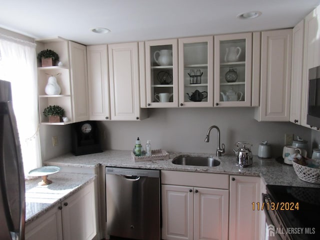 kitchen with light stone counters, a sink, dishwasher, open shelves, and glass insert cabinets