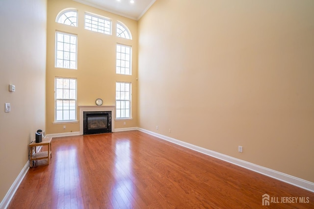 unfurnished living room with wood finished floors, baseboards, ornamental molding, a towering ceiling, and a high end fireplace