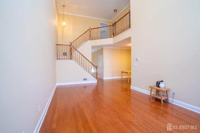 unfurnished living room featuring a high ceiling, stairway, crown molding, baseboards, and wood finished floors