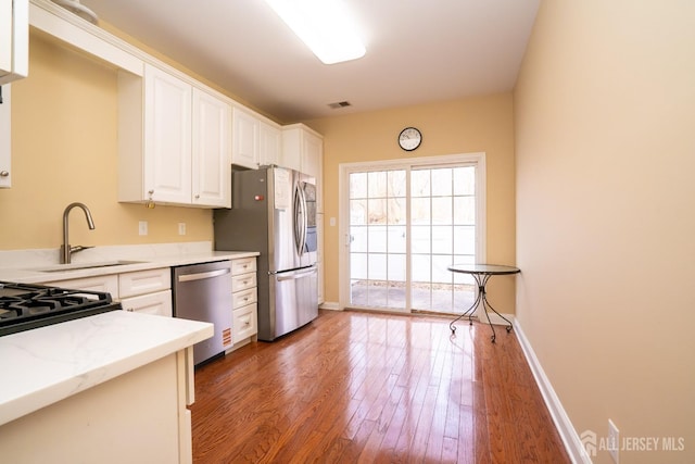 kitchen featuring a sink, wood-type flooring, visible vents, white cabinetry, and appliances with stainless steel finishes