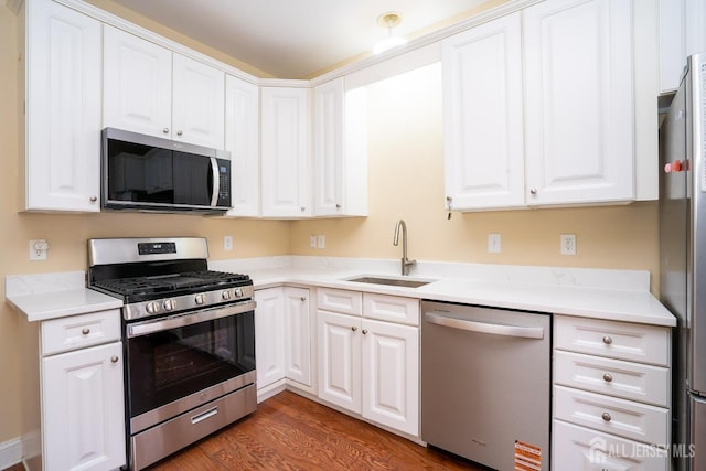 kitchen featuring wood finished floors, stainless steel appliances, light countertops, white cabinets, and a sink