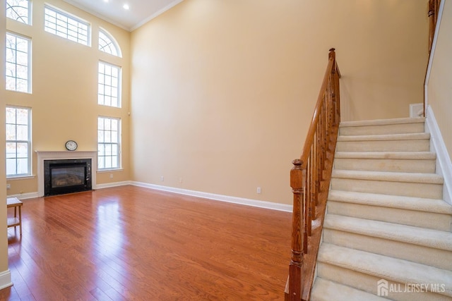 unfurnished living room with a high ceiling, stairway, baseboards, ornamental molding, and wood finished floors