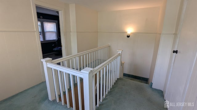 hall featuring an upstairs landing, carpet, wainscoting, and a decorative wall