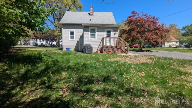 back of house featuring a chimney, a lawn, and roof with shingles